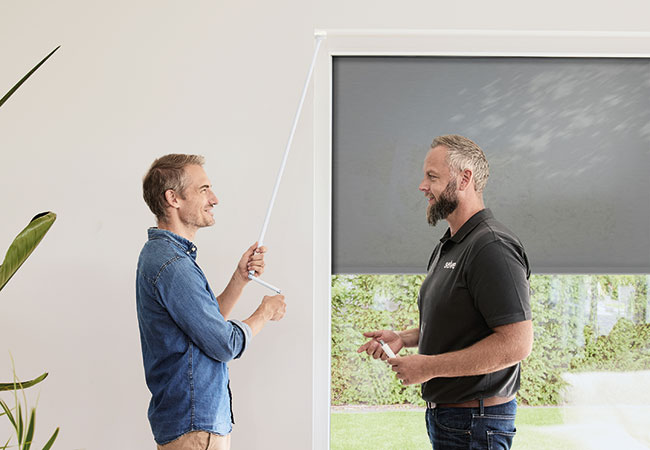 SELVE Berater und Kunde stehen am Fenster, Kunde bedient die Handkurbel mit dem Freilauf